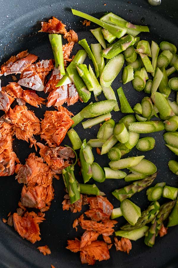 salmon pieces with chopped asparagus in a skillet