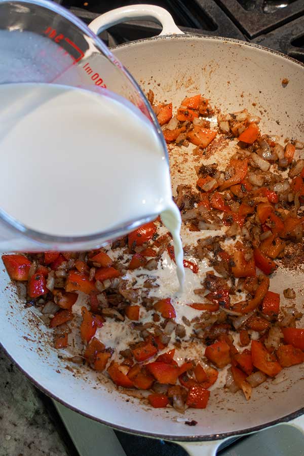 adding cream to bell peppers and onions cooking in a skillet