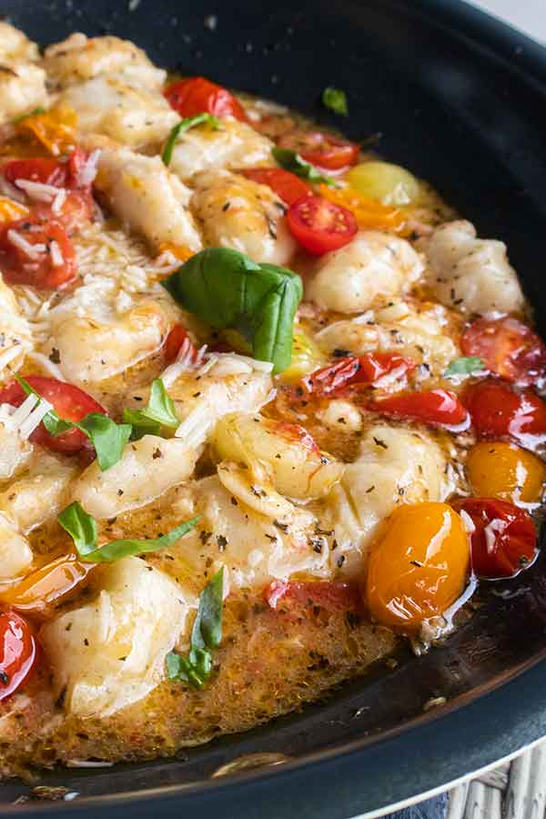 close up of cheesy gnocchi in a pan with cherry tomatoes