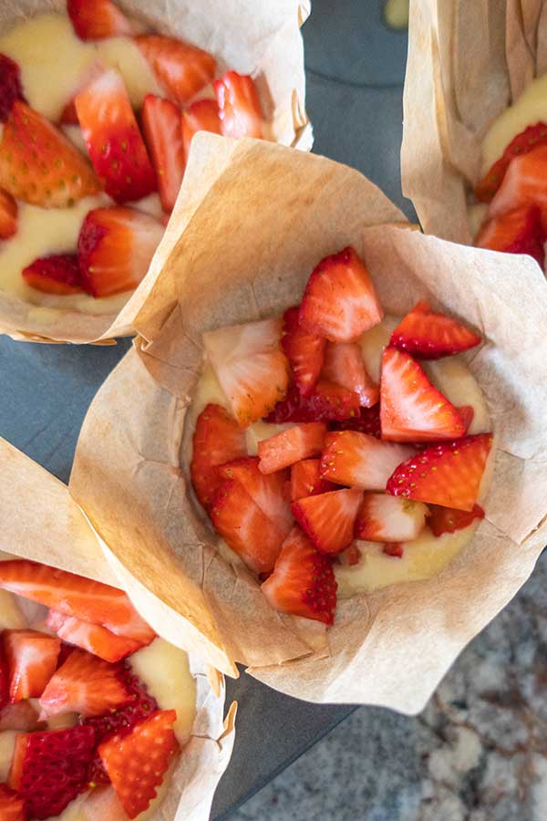 muffin batter in muffin cups topped with fresh strawberries