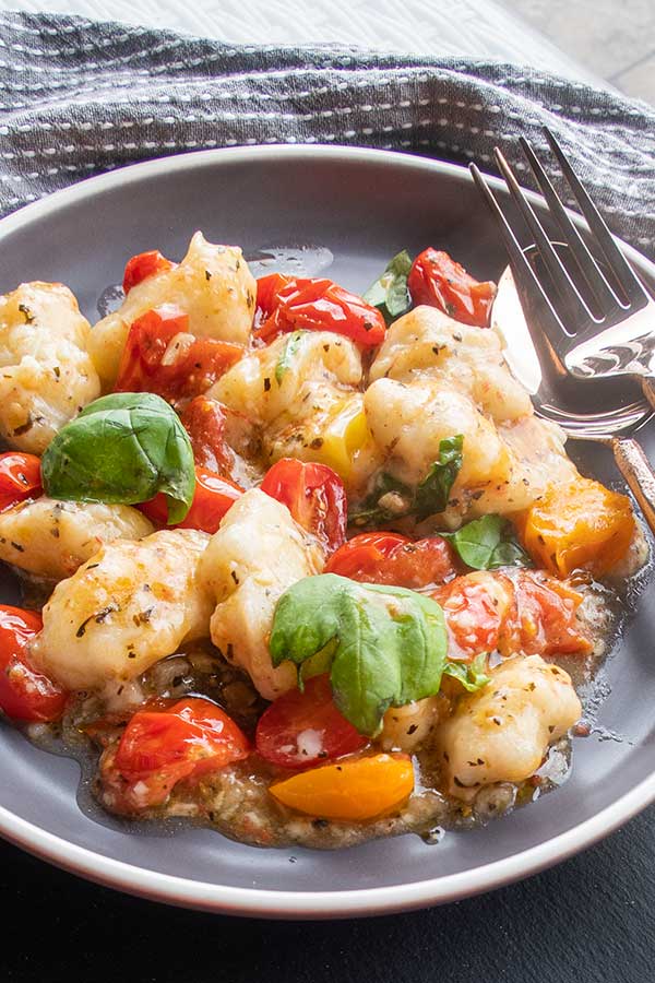 gluten free dumplings in a cheesy sauce on a plate with cherry tomatoes and basil