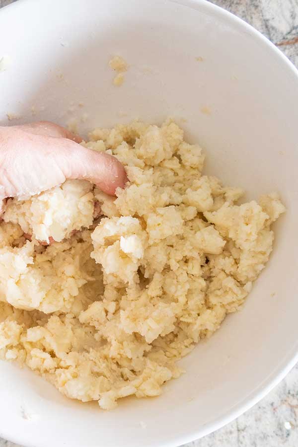 using a hand to mix mashed potatoes with cheese and sesame seeds in a bowl
