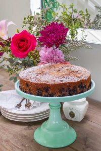blueberry cake on a cake stand with flours in a vase