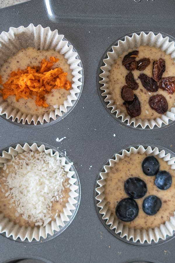 muffin batter topped with carrots, berries and coconut in a pan