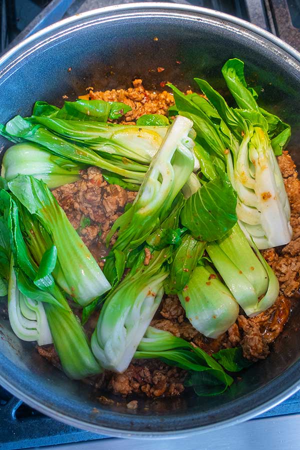 sambal pork sauce simmering with bok choy in a saucepan