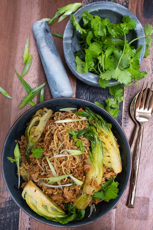 top view sambal pork in a skillet and cilantro in a mortar