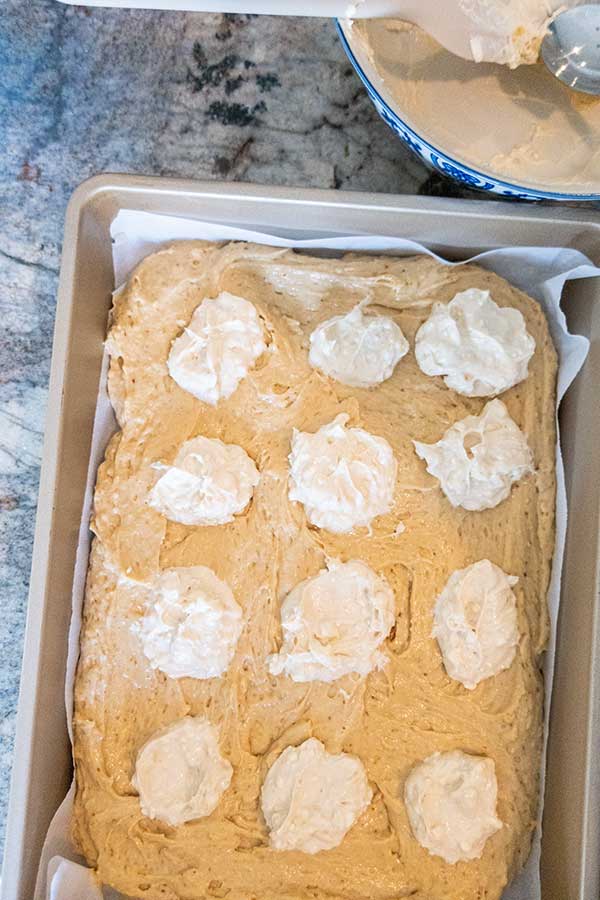 coffee cake batter in a cake pan topped with dollops of cream cheese