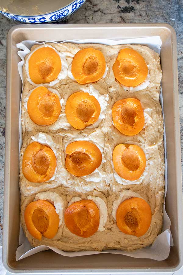 cake batter in a pan topped with dollops of cream cheese and halved apricots
