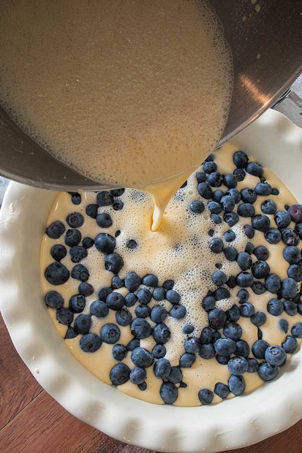 batter pouring over blueberries into a pie dish