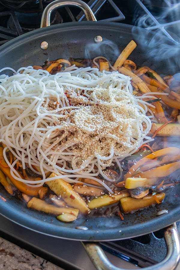 adding noodles to veggies in a skillet