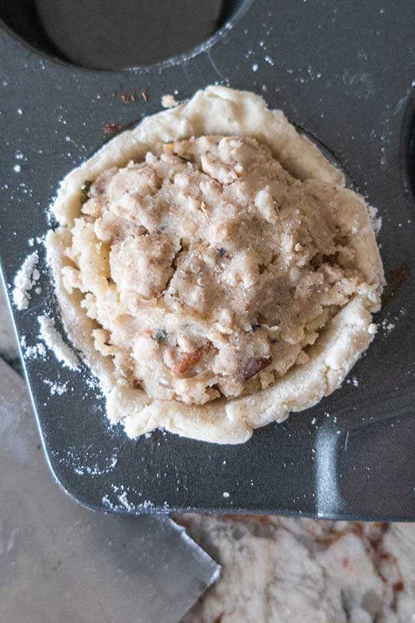 uncooked shortcrust pastry with meat filling in a muffin cup