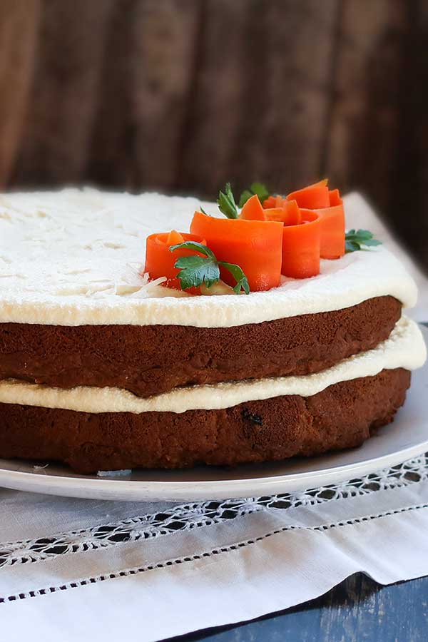 2 layer vegan gluten free carrot cake with frosting and carrot roses on a cake platter