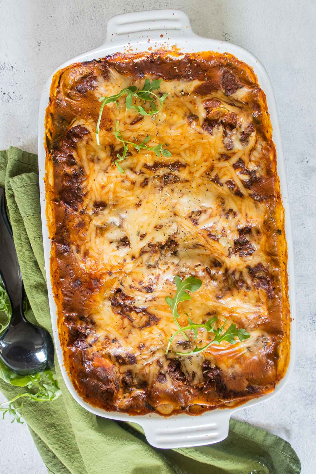 overview of baked lasagna in a baking dish topped with dairy free cheese and greens