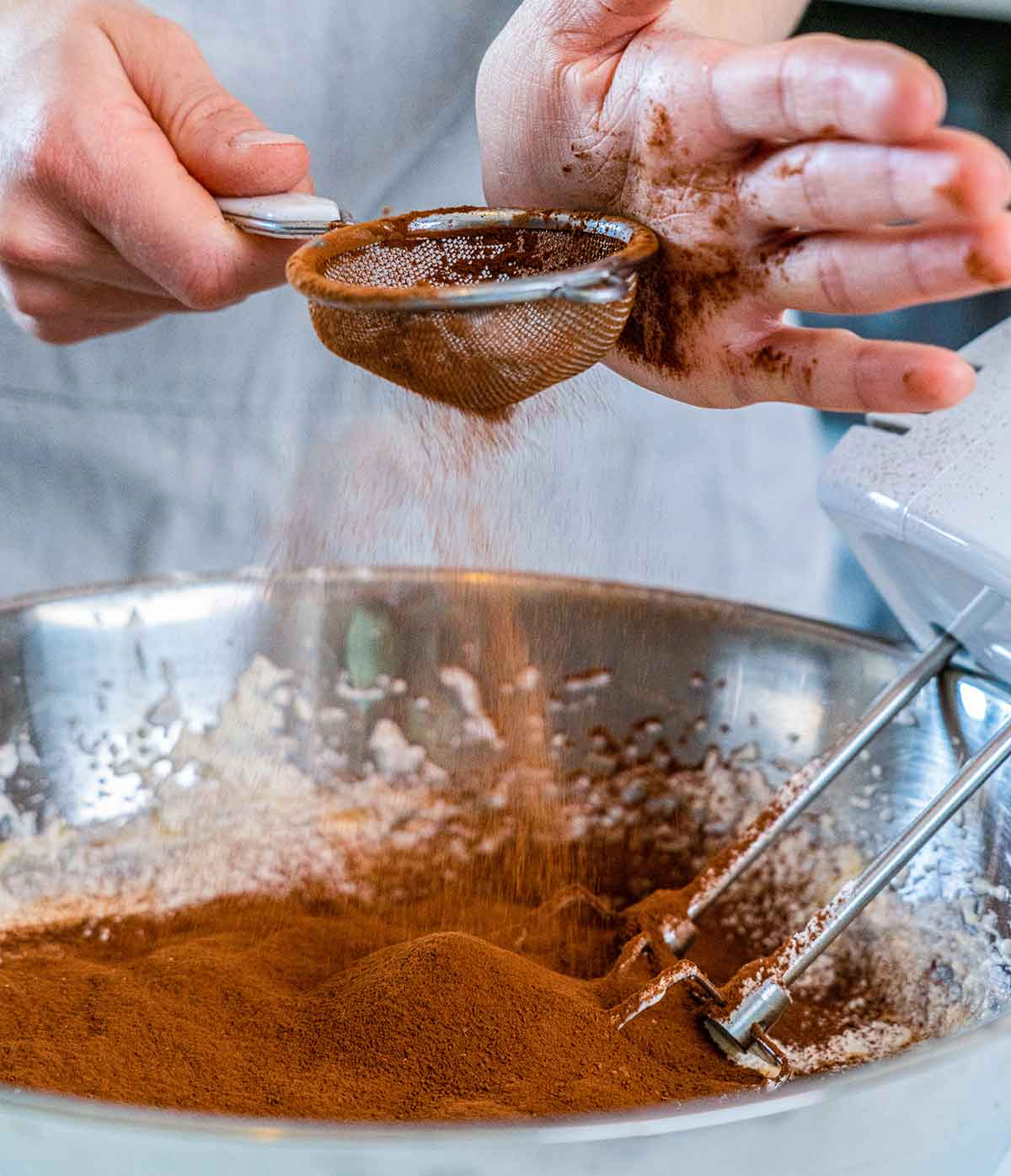 using hands to sieve cocoa powder into a bowl
