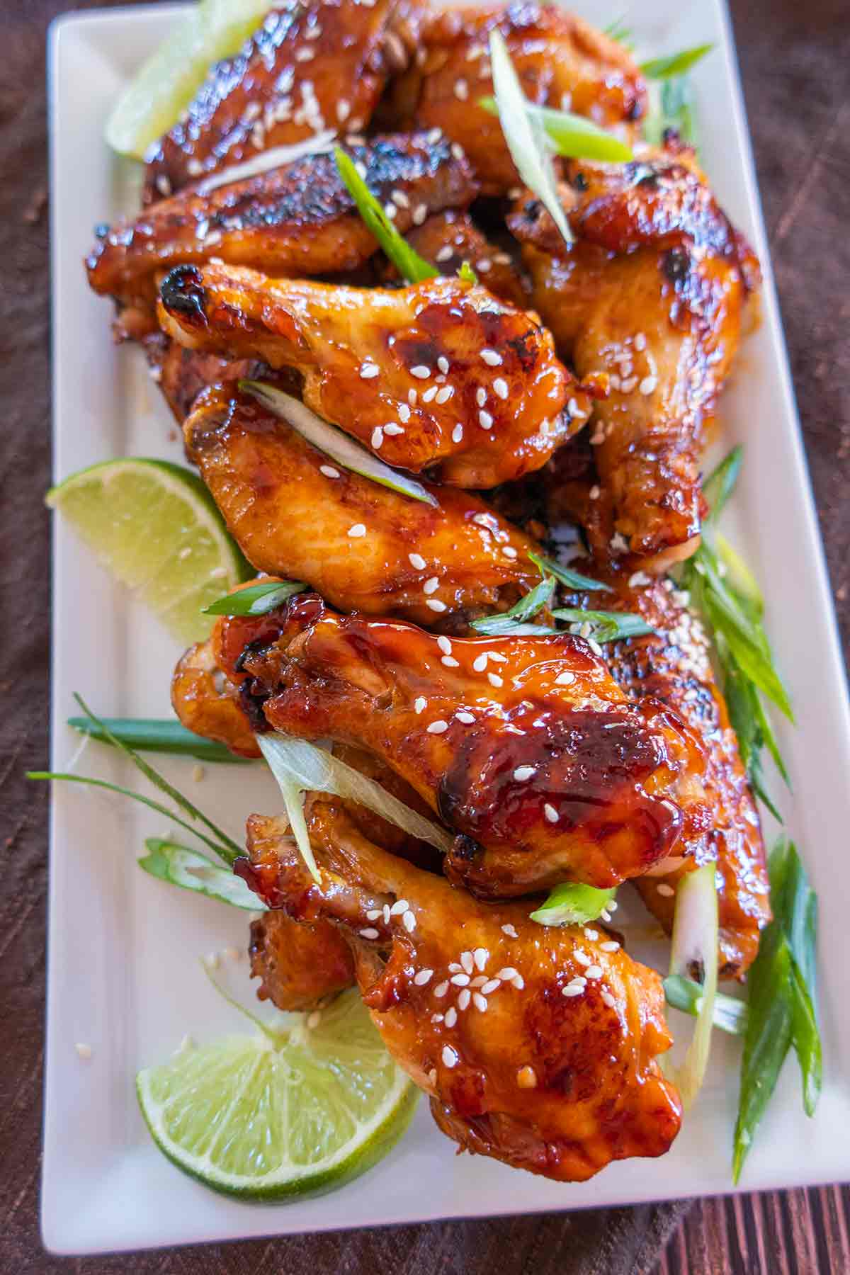 overview of baked wings with sesame seeds, green onions and lime wedges