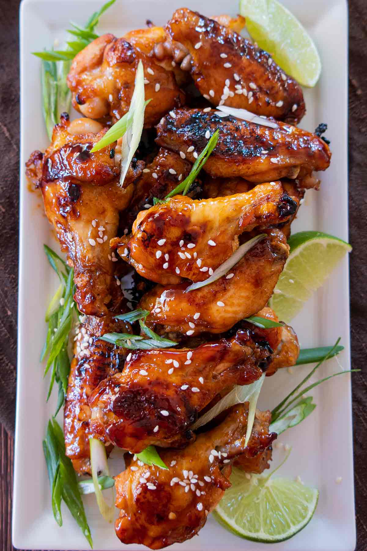 baked korean chicken wings topped with green onions, sesame seeds and lime wedges on a platter