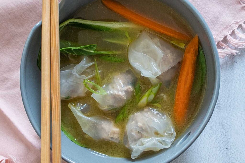 wonton soup with dumplings, bok choy and carrots in a bowl