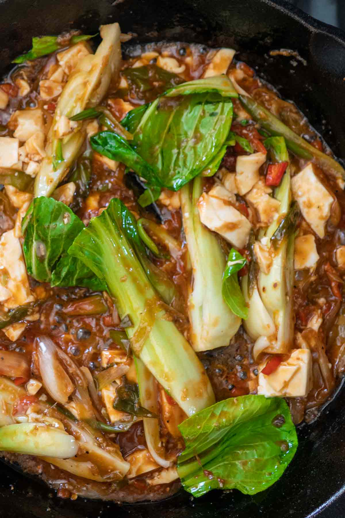 bok choy and cubed tofu cooking in a skillet with schezwan sauce