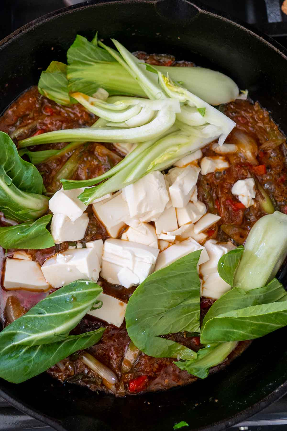 bok choy and cubed tofu added to schezwan sauce in a skillet