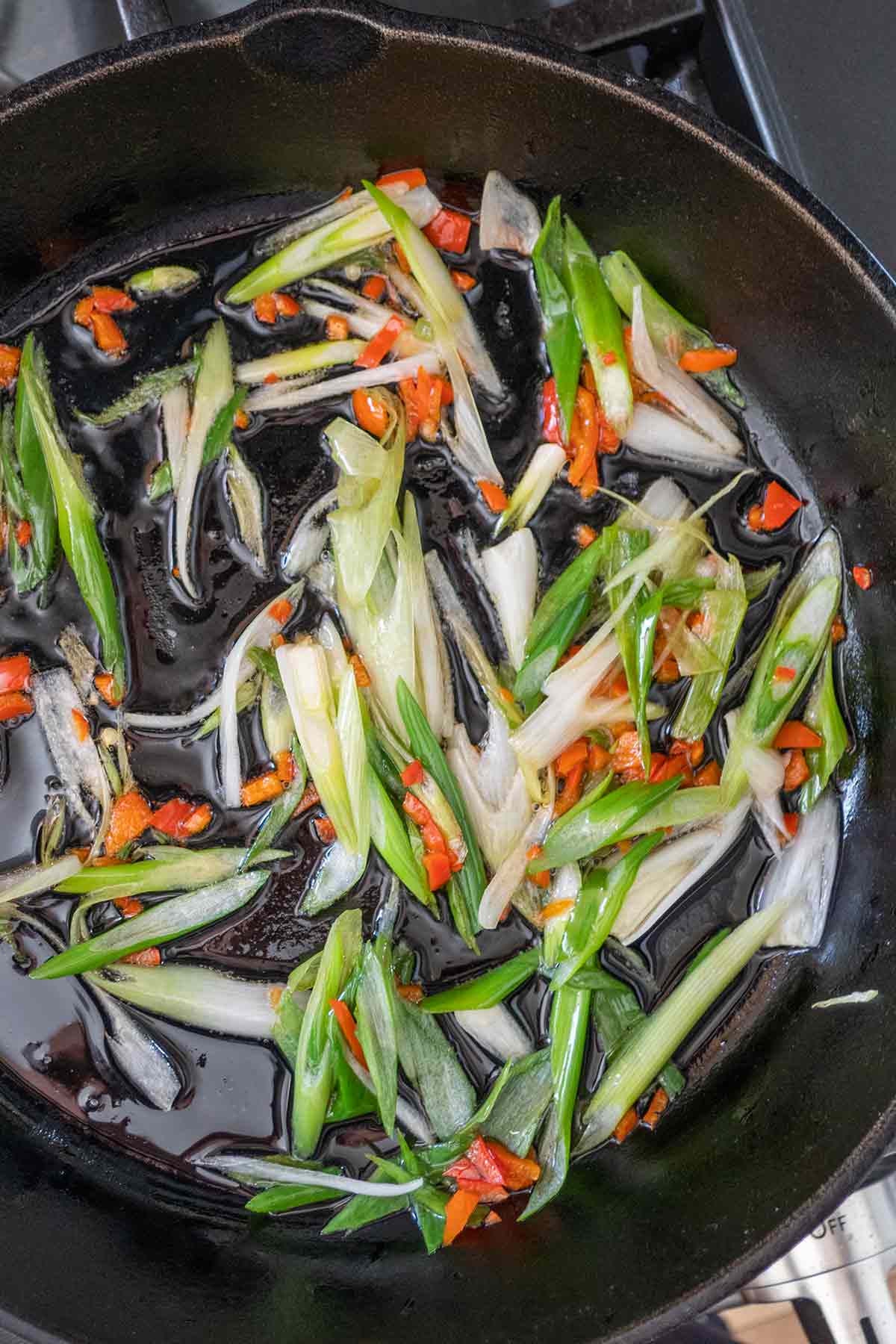 sliced green onions and fresno peppers cooking in sesame oil in a skillet