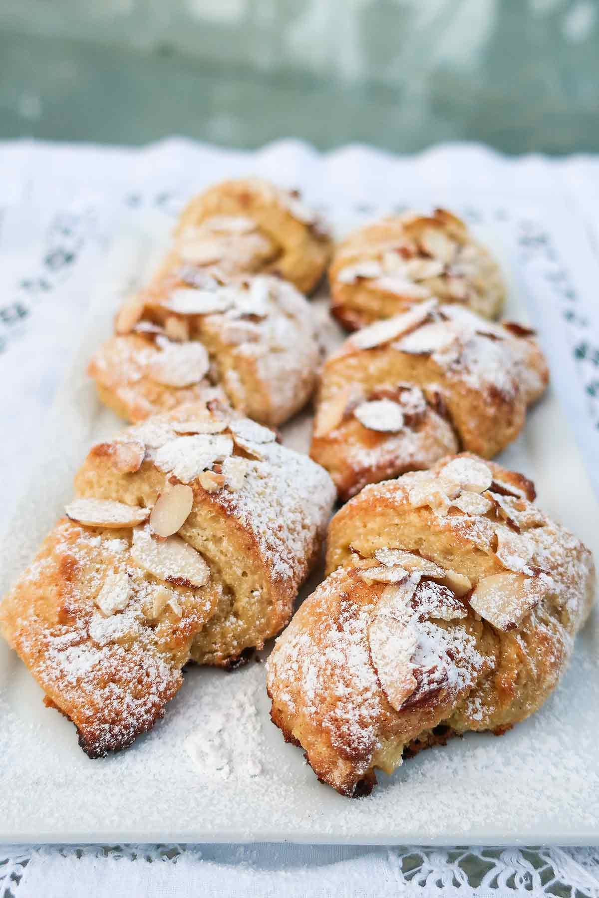 almond crescent rolls topped with sliced almonds and powdered sugar on a dessert tray 