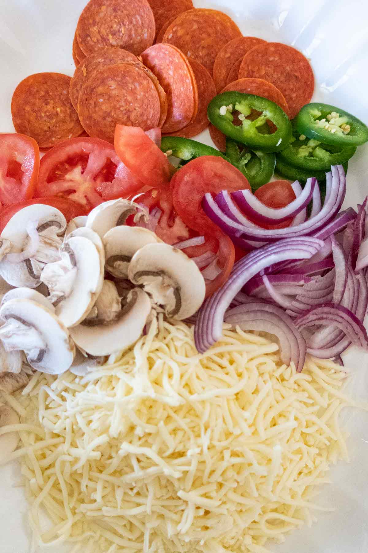 sliced pepperoni, onions, mushrooms, tomatoes, jalapenos and cheese on a plate