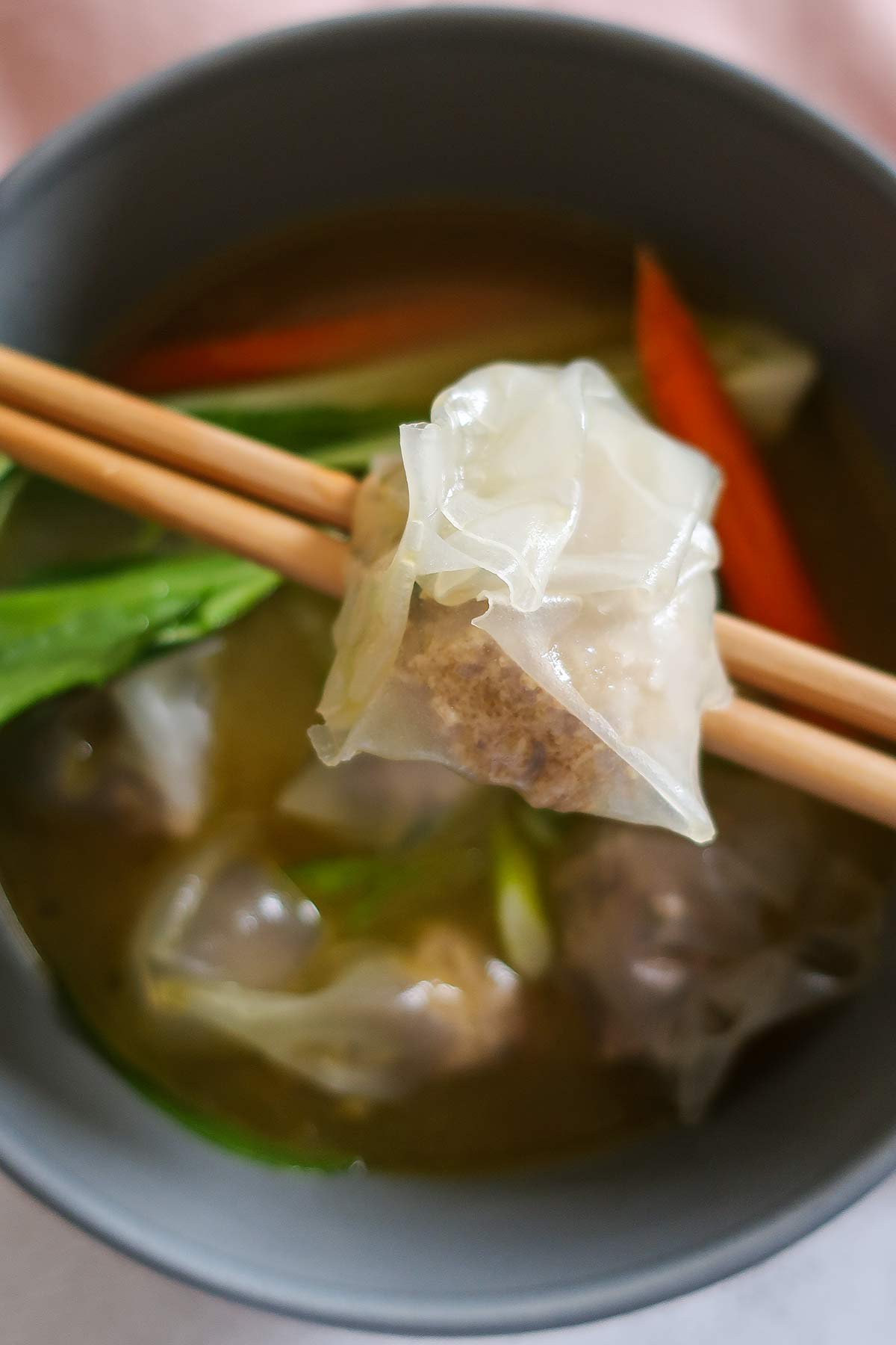 gluten free cooked wonton on chopsticks over a bowl of soup