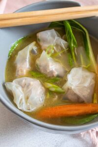 a bowl of soup with wontons, bok choy and chopsticks