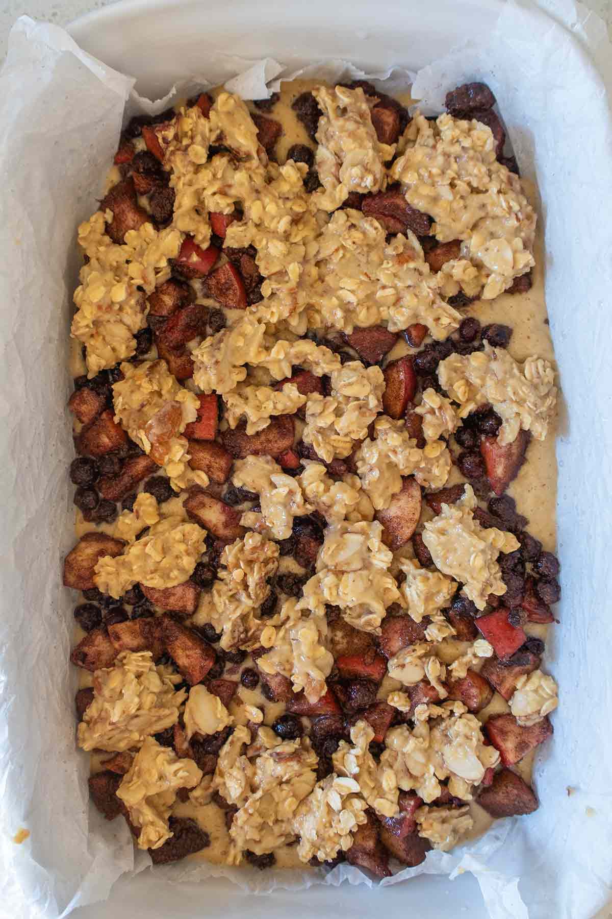 gluten free bar batter topped with fruit and oat topping in a pan before baking