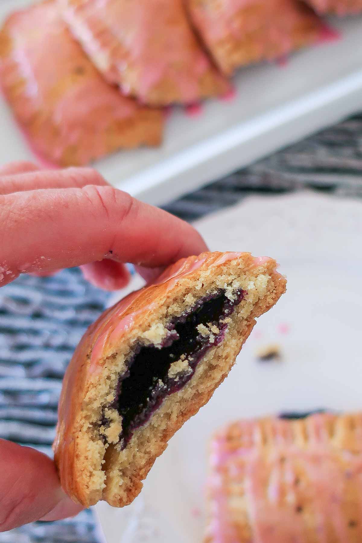 a hand holding half a gluten free pop tart exposing blueberry filling