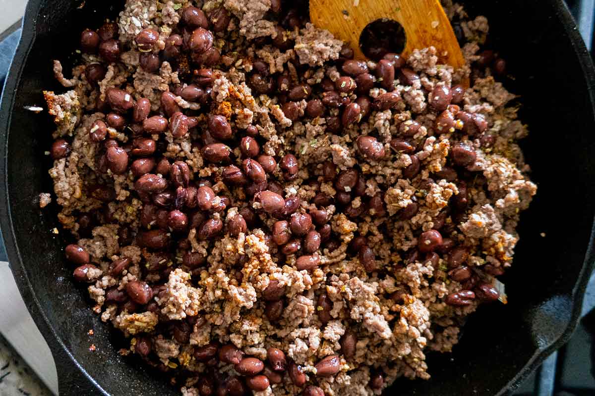 browned ground beef with black beans and seasoning in a cast iron skillet