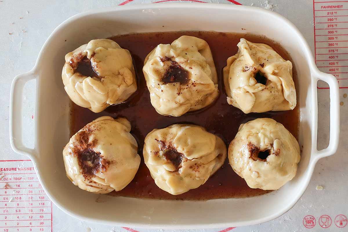 unbaked 6 apple dumpings with sauce in a baking dish