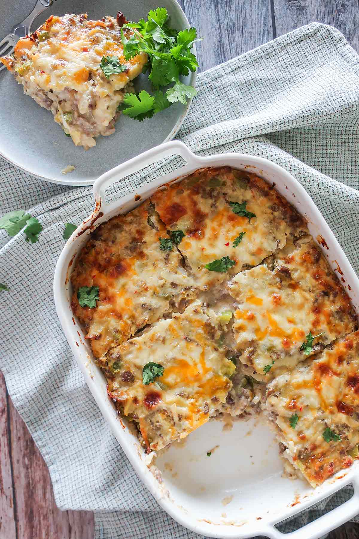 a slice of sausage breakfast casserole missing in a baking dish with a side plate