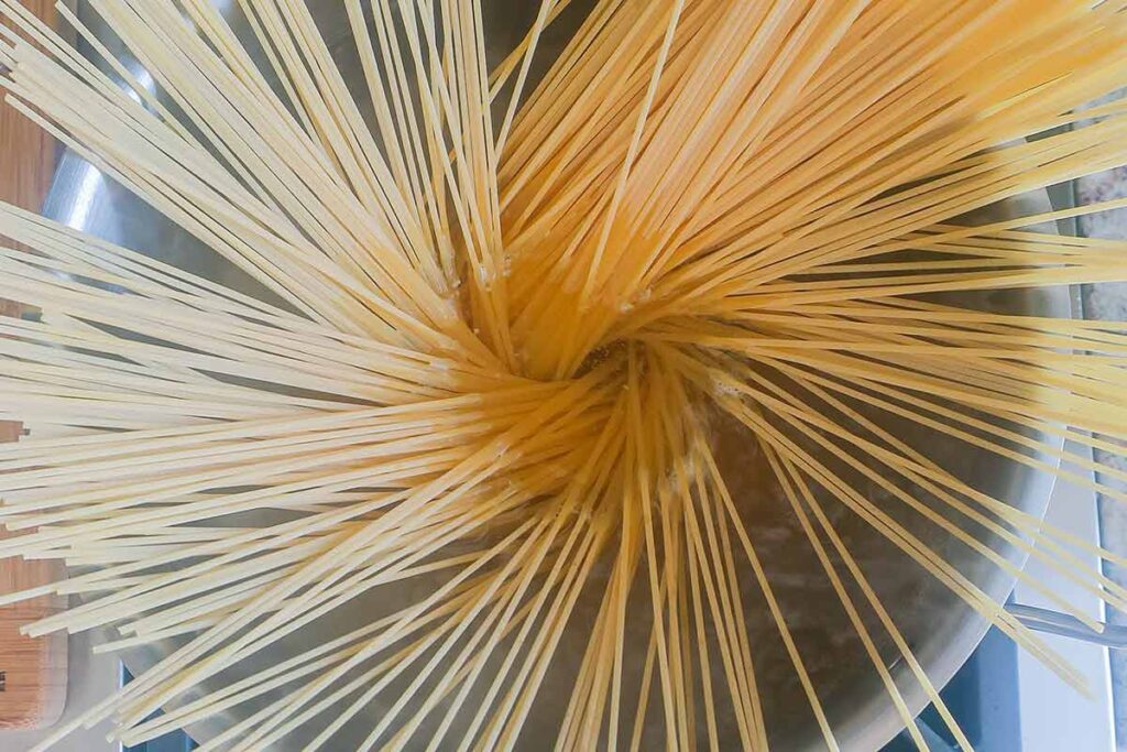showing dropped dry spaghetti pasta in a pot of boiling water