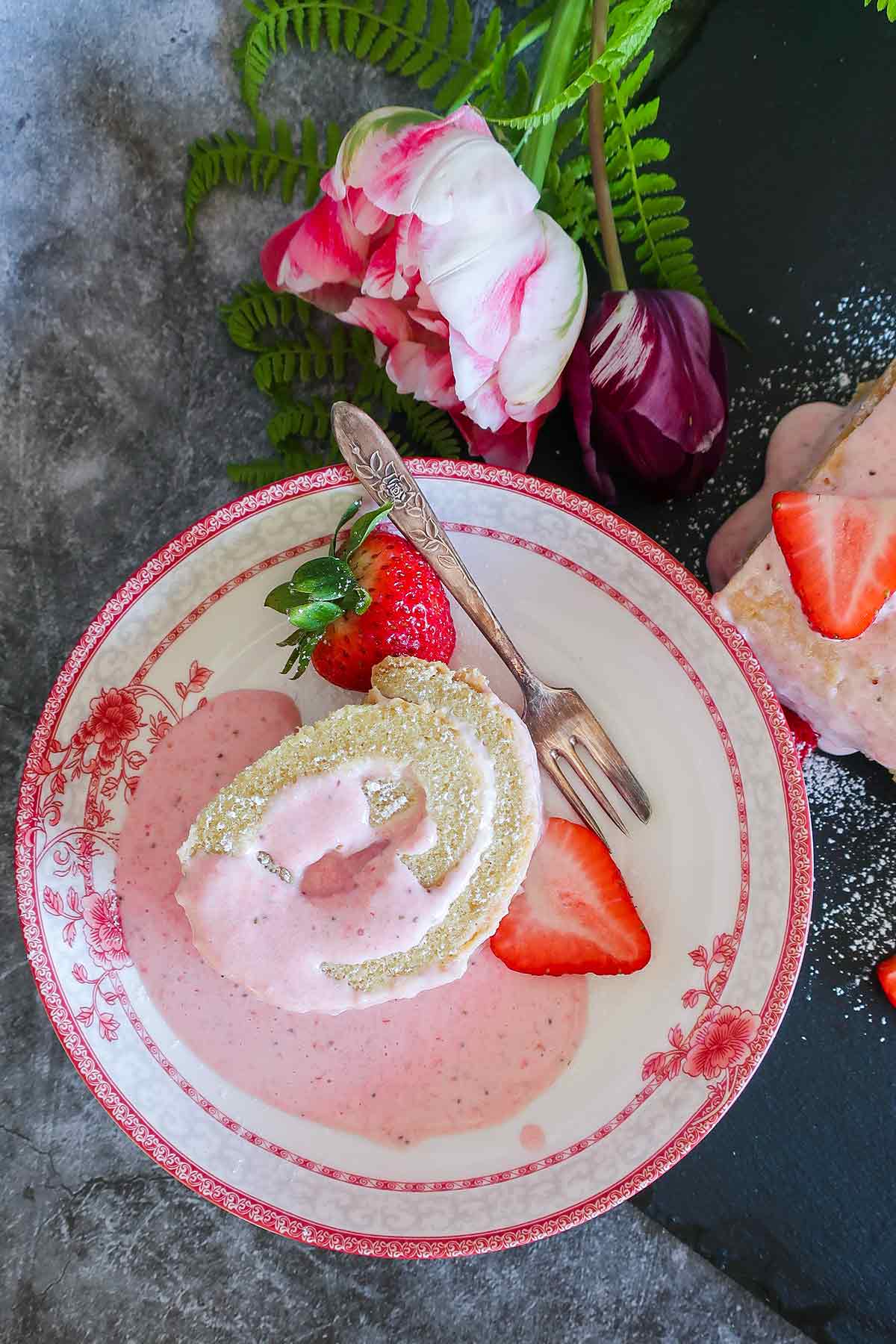 a slice of strawberry cheesecake swiss roll on a plate with strawberries