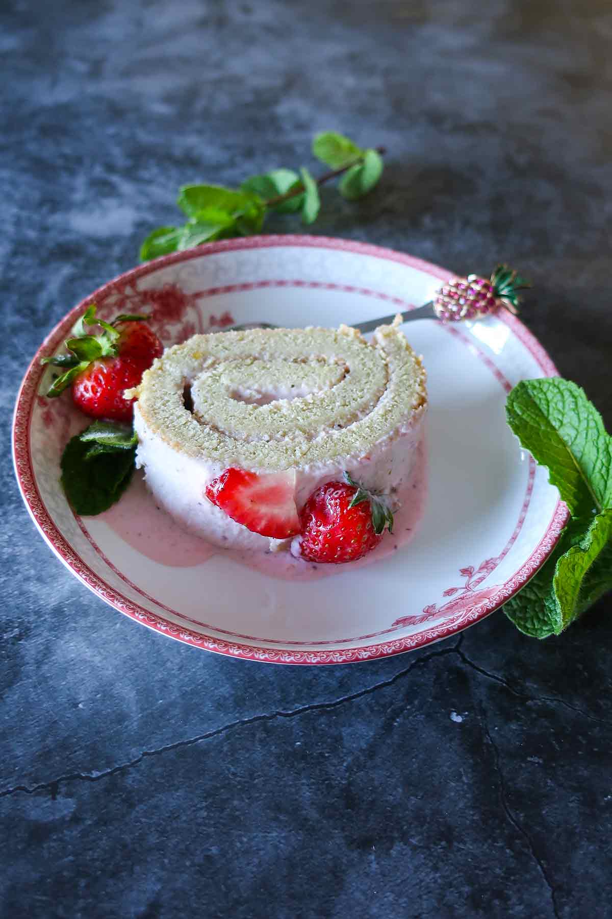 a slice of gluten free jelly roll garnished with mint and strawberries on a plate