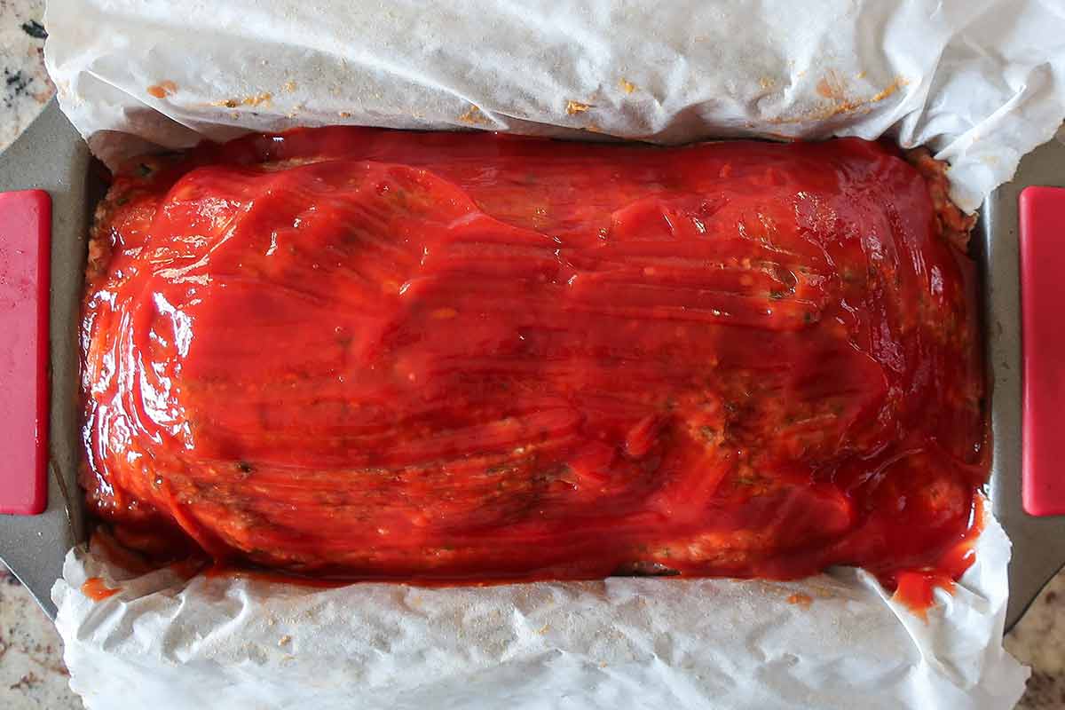 overview of uncooked meatloaf in a loaf pan brushed with ketchup and brown sugar