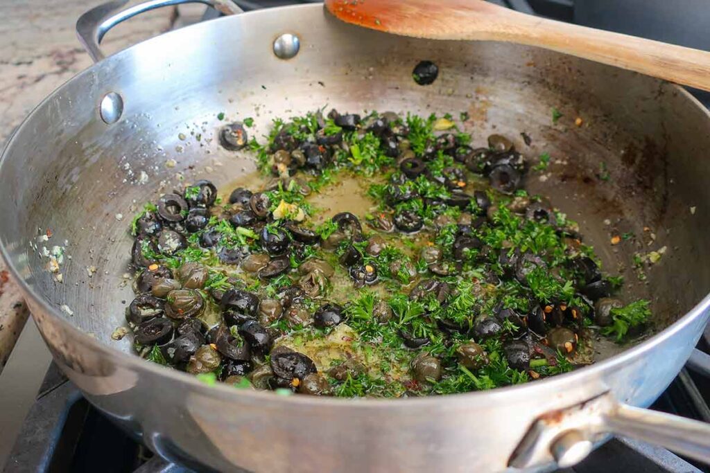olive oil, garlic, anchovies, capers, olives and parsley cooking in a skillet