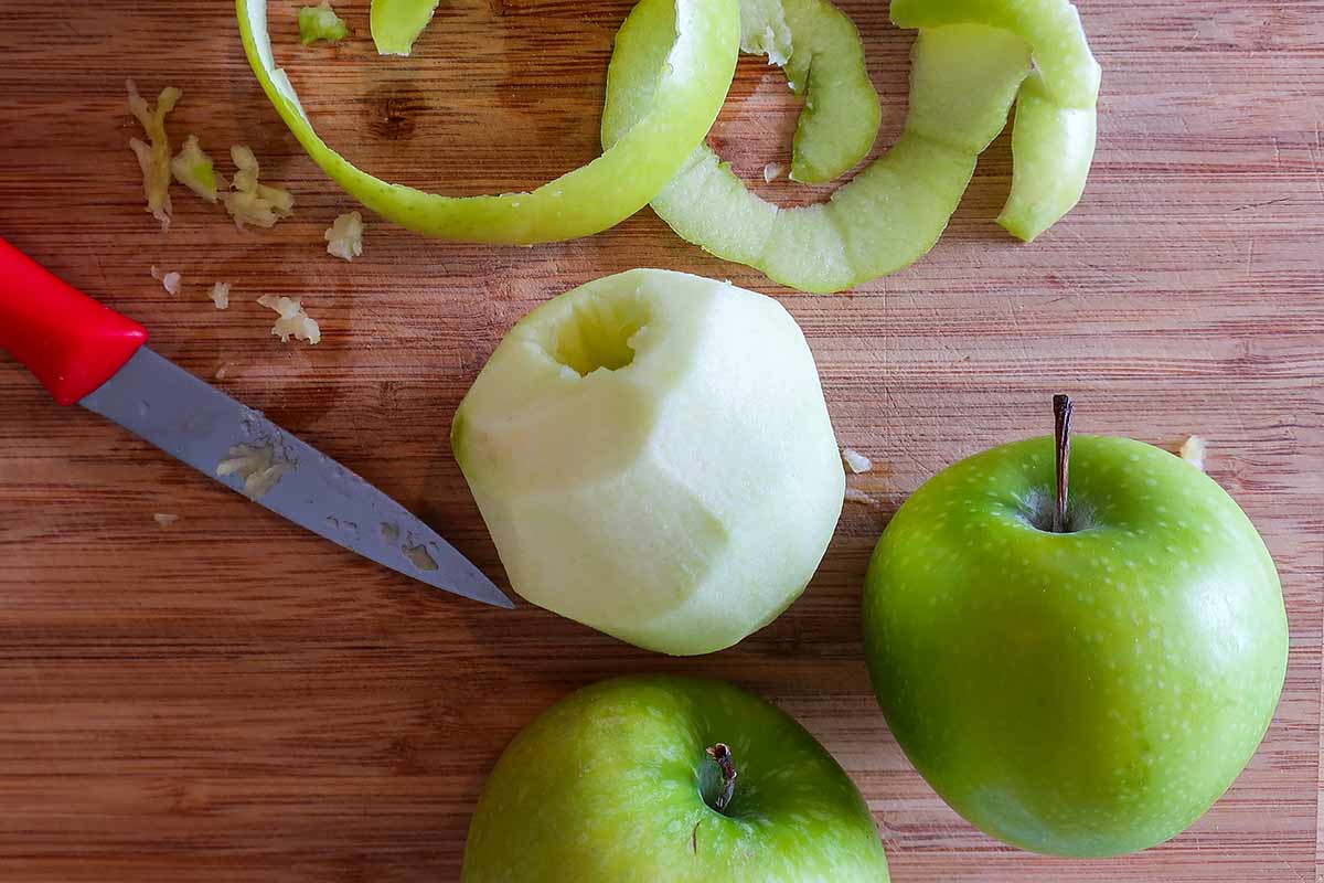 cored and peeled apple on a wooden cutting board with a paring knife