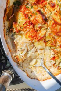 dish with scalloped potatoes and a spoon showing the sauce