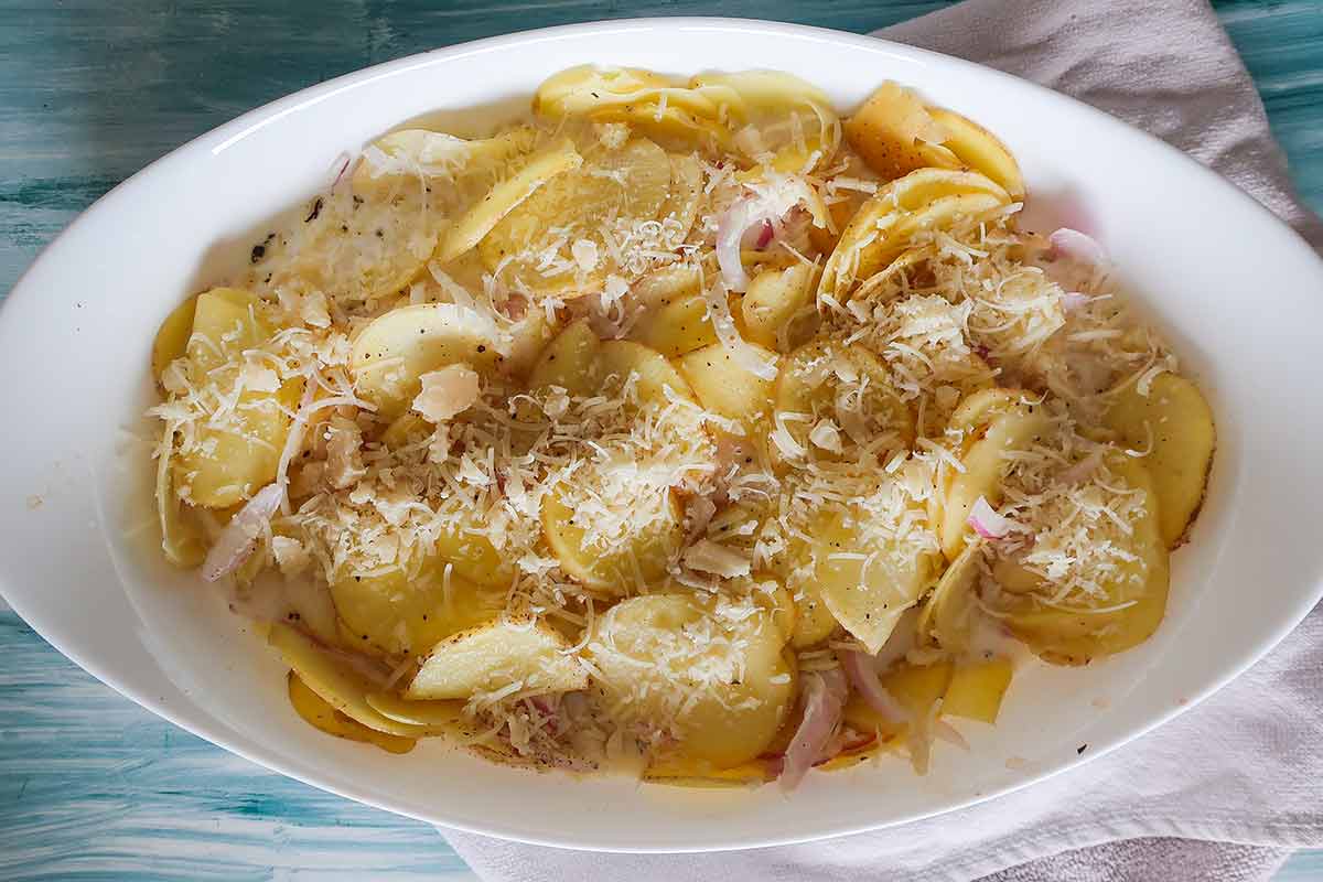 uncooked layered potatoes with onions with white sauce in a casserole dish