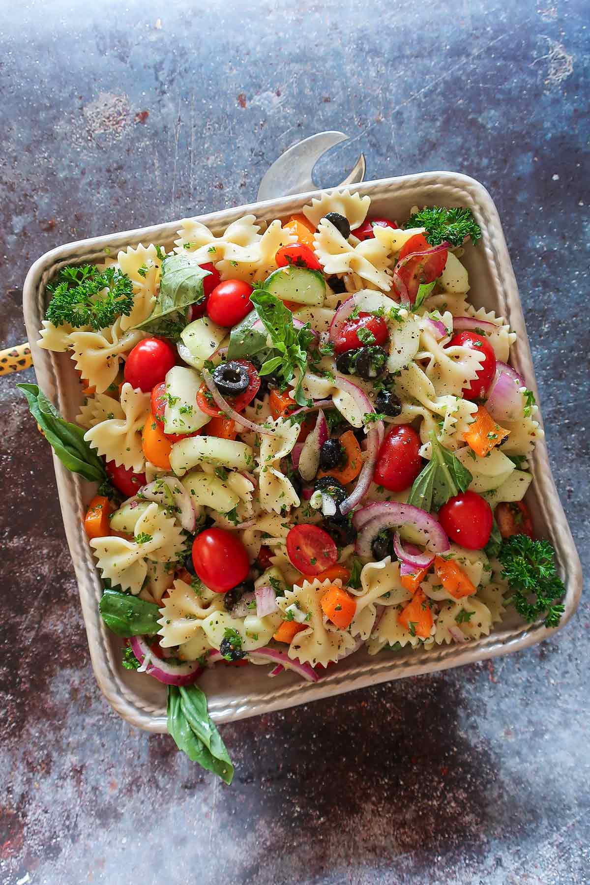 gluten free pasta, tomatoes, peppers, cucumber, olives, onions and herbs in a bowl