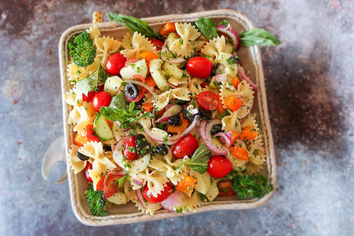 best summer pasta salad with olives, tomatoes, onions and herbs in a bowl
