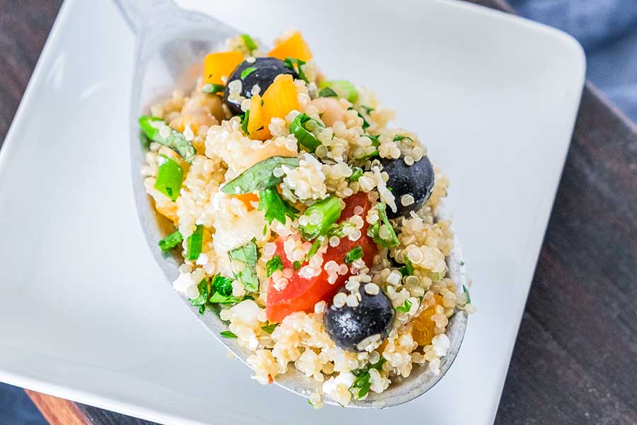 greek quinoa salad with olives, tomatoes and herbs on a large spoon