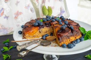 Fresh apricot and blueberry gluten-free tarte Tatin on a dessert platter with two spoons, showing juicy caramelized fruit filling and fresh blueberries—an ideal summer dessert.