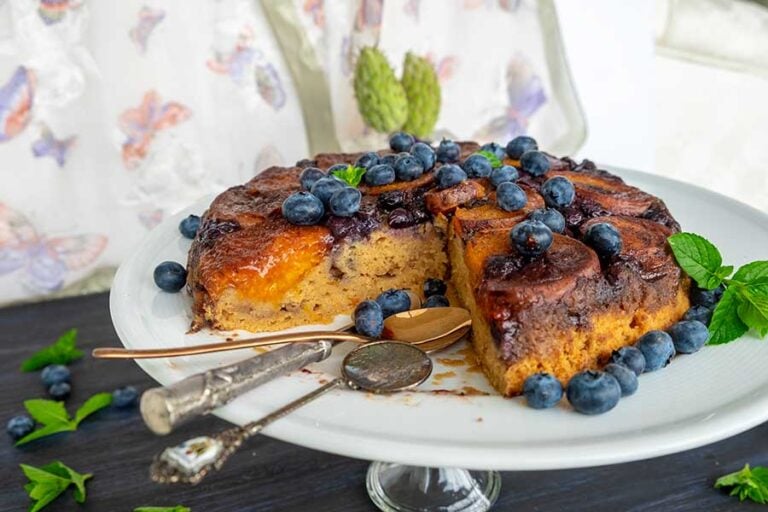 Fresh apricot and blueberry gluten-free tarte Tatin on a dessert platter with two spoons, showing juicy caramelized fruit filling and fresh blueberries—an ideal summer dessert.