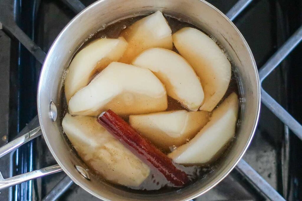 fresh quartered pairs in flavored water with cinnamon stick in a saucepan