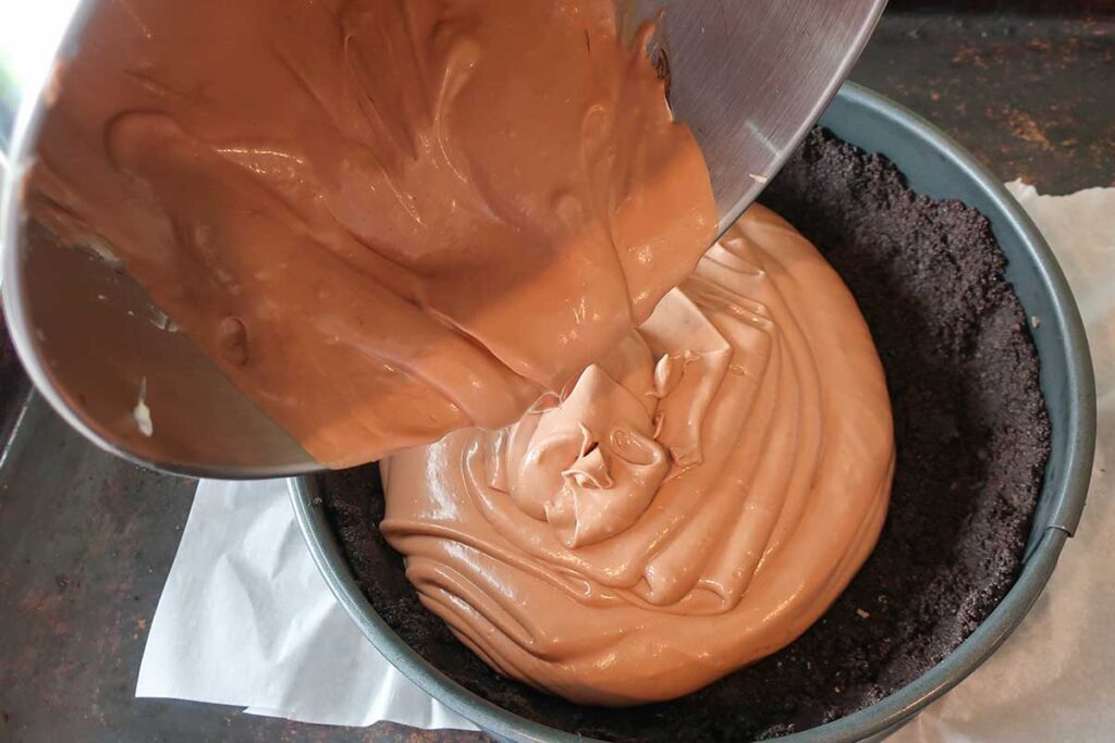 pouring cheesecake filling into the oreo cookie crust in a springform pan