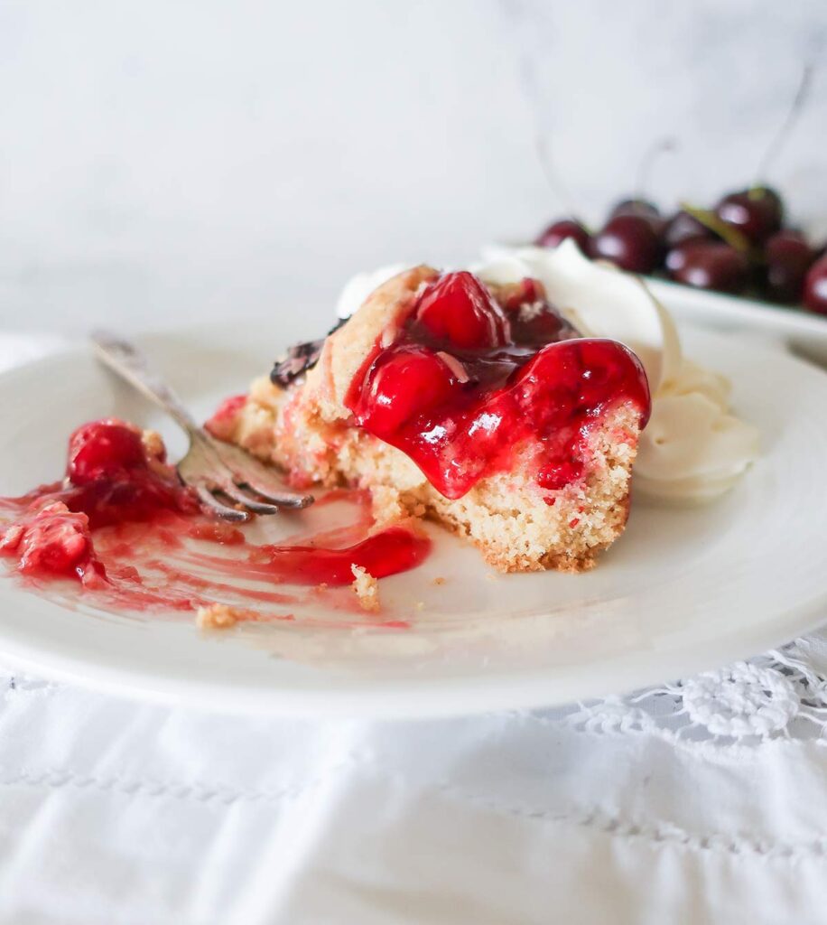 half a slice of cherry cake on a plate with a fork