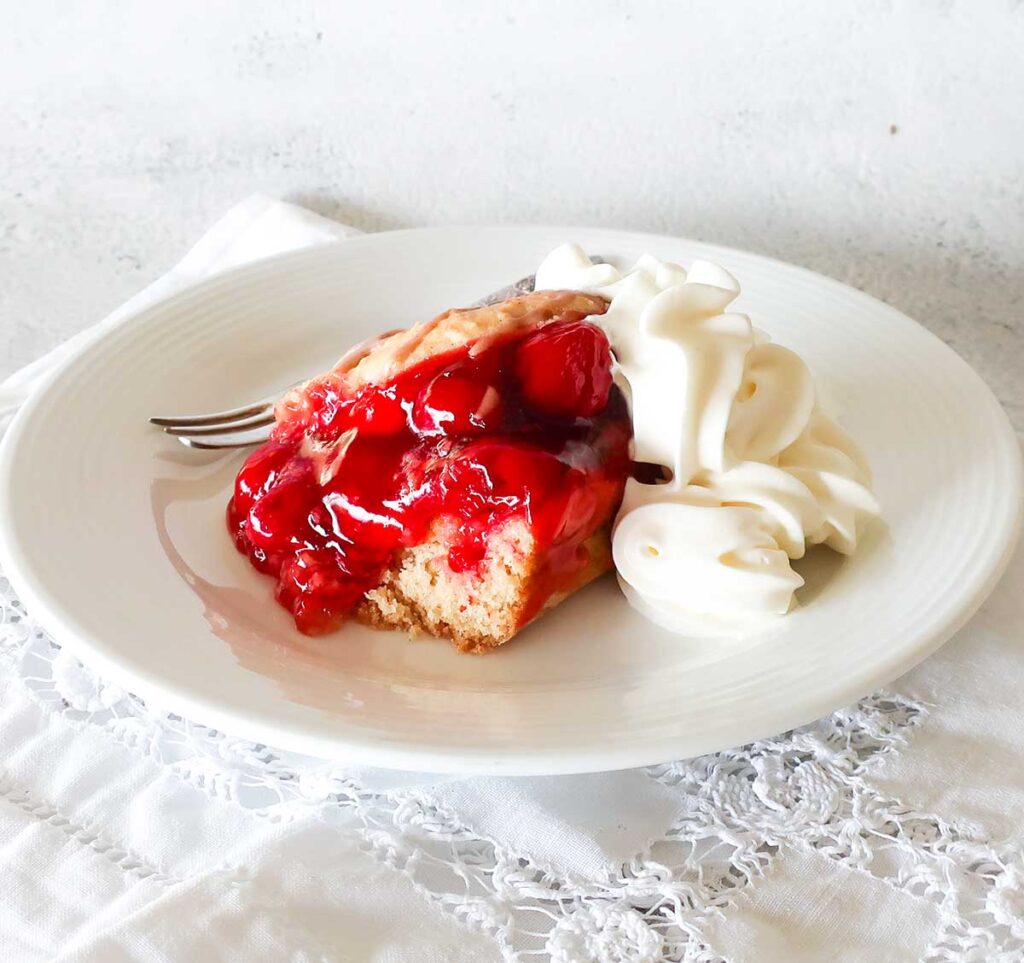 showcasing the cherry pie filling in a cherry cake on a plate with whipped cream